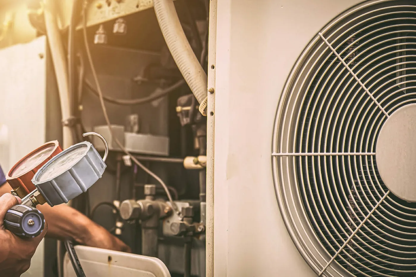 Une personne du métier contrôle le circuit frigorifique d’une pompe à chaleur avec deux manomètres, à droite le ventilateur de l’appareil
