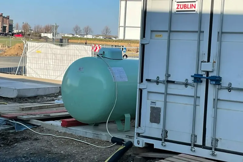 Flüssiggastank auf Betonplatte neben einem Heizcontainer auf der Baustelle